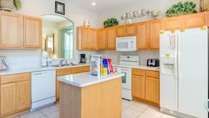 A modern kitchen with wooden cabinets, a central island, a white refrigerator, and a microwave. - Ov535 - Emerald Island - 7 Bed 4 Baths Villa (Kissimmee)