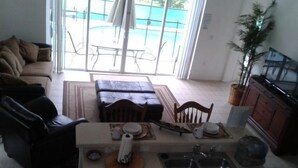 Una sala de estar con un sofá, una mesa de centro y una mesa de comedor con sillas. Hay una zona de cocina con un lavamanos y armarios.