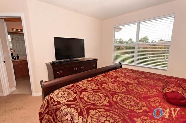 A bedroom with a large bed, a TV on a dresser, and a window with blinds.