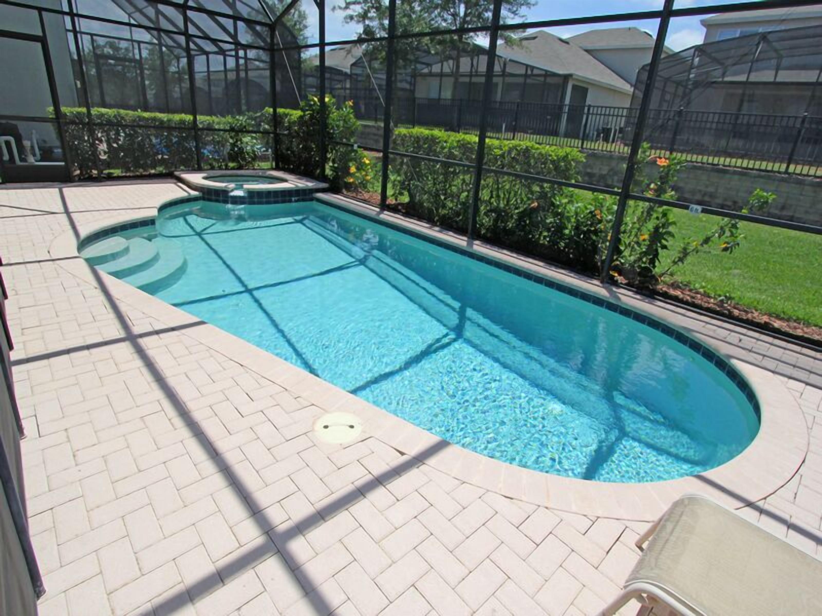 A rectangular swimming pool with a hot tub, surrounded by a brick patio and a glass enclosure.