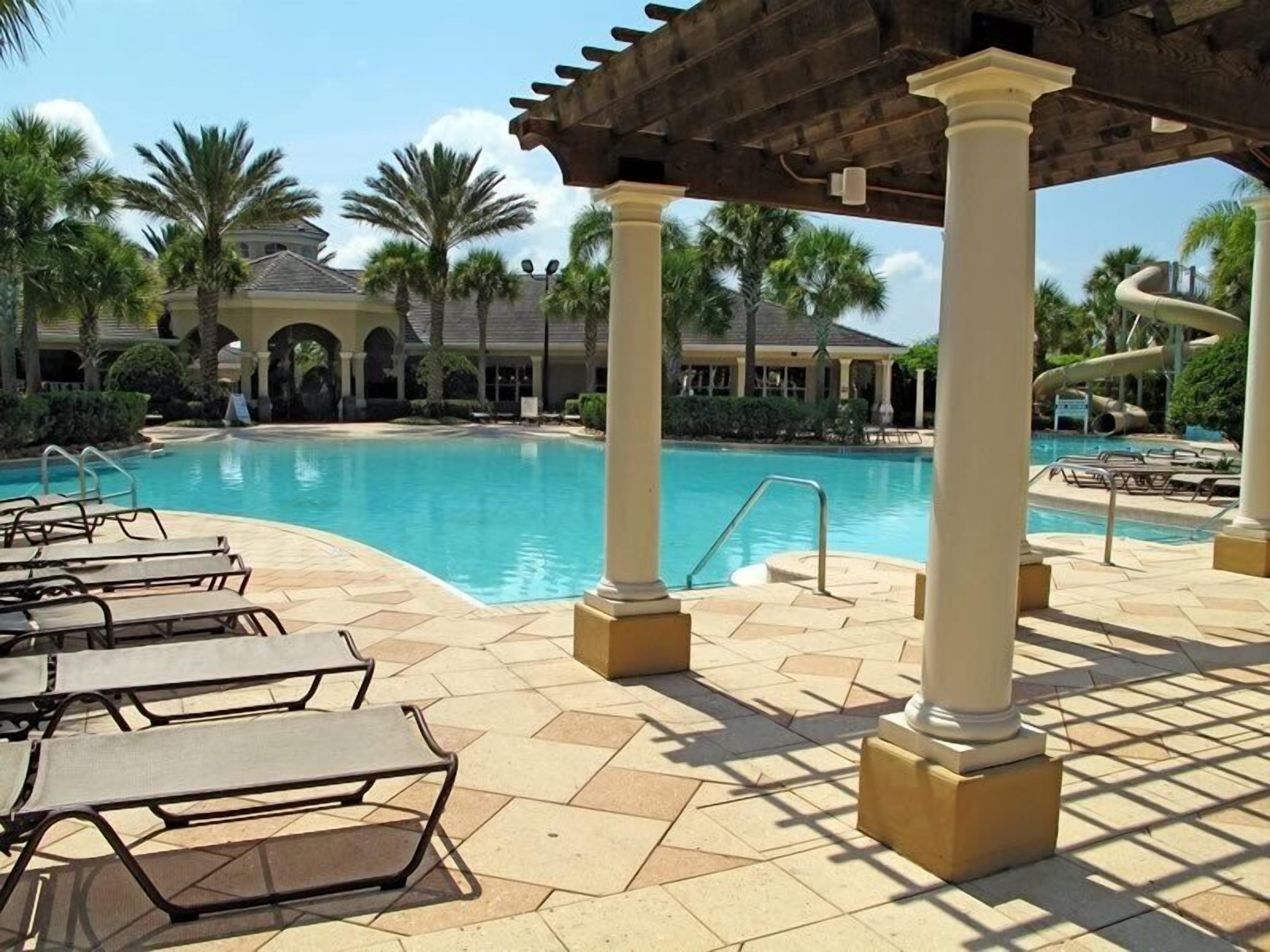 A pool area with lounge chairs, a covered seating area, and a water slide in the background.