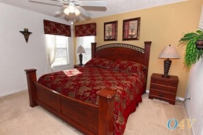 A bedroom with a wooden bed, a ceiling fan, a nightstand, a lamp, and a plant.