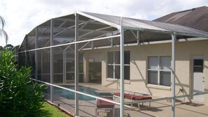 A covered outdoor area with a pool, lounge chairs, and a house in the background. - Ov2287 - Espirit - 3 Bed 2 Baths Villa (Davenport)