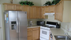 A kitchen with wooden cabinets, a stainless steel refrigerator, a coffee maker, a microwave, a stove, and a sink. - Ov2287 - Espirit - 3 Bed 2 Baths Villa (Davenport)
