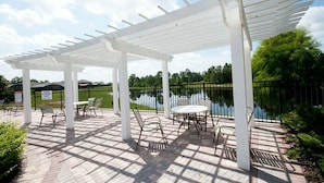 Un patio couvert agrémenté d’une pergola blanche, de meubles d’extérieur et offrant une vue sur un lac.