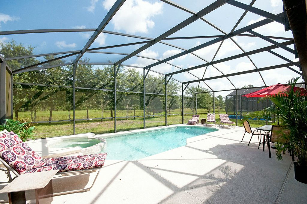 A covered outdoor swimming pool area with lounge chairs and a hot tub, surrounded by a metal frame and glass panels.