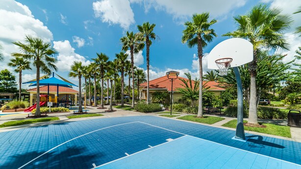 An outdoor basketball court with a blue surface, surrounded by palm trees and a building with a red roof. - Ovm1754 - Terra Verde Resort - 4 Bed 3 Baths Townhome (Kissimmee)