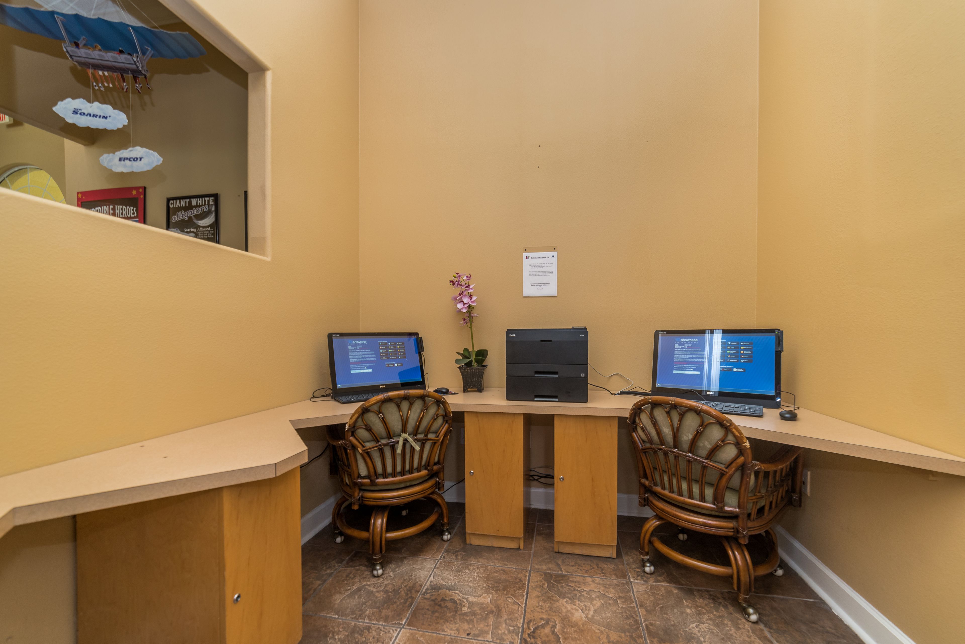 A small office with two computers, wicker chairs, and a potted plant.