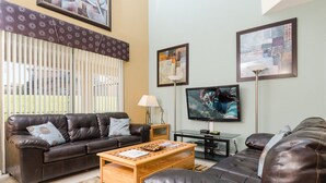 A living room with a brown leather sofa, a wooden coffee table, and a TV on a stand. - Ov1138 - Emerald Island - 7 Bed 4.5 Baths Villa (Kissimmee)