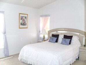 A bedroom with a large bed, a nightstand with a lamp, a framed picture on the wall, and a window with curtains. - Ov2498 - Loma Vista - 4 Bed 3 Baths Villa (Davenport)