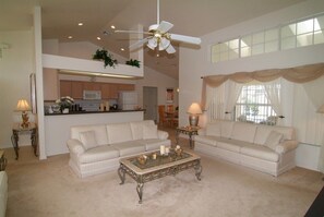 A spacious living room with two striped sofas, a glass coffee table, and a ceiling fan. A kitchen is visible in the background. - Ov2498 - Loma Vista - 4 Bed 3 Baths Villa (Davenport)