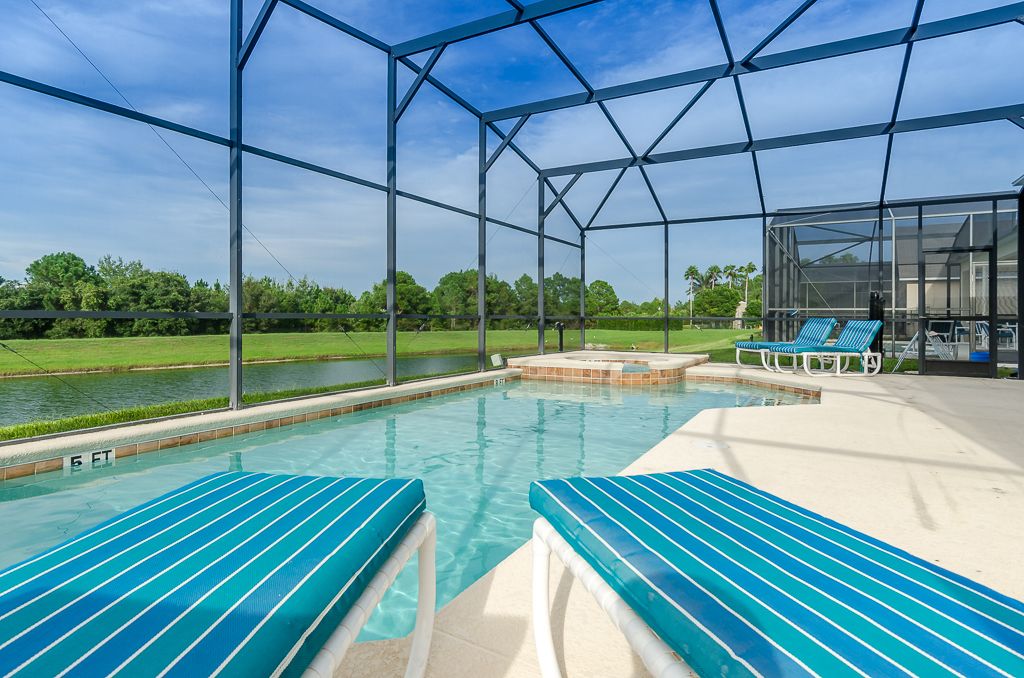 A swimming pool with blue-striped lounge chairs and a covered area with a glass enclosure.