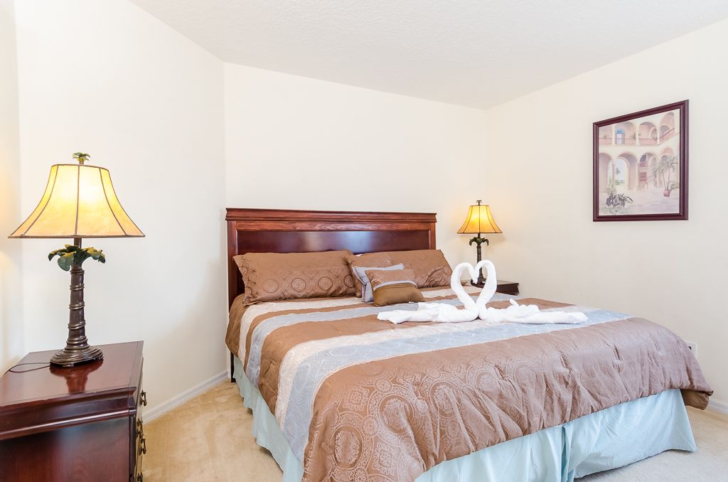 A neatly made bed with a brown headboard, two bedside lamps, and a framed picture on the wall.