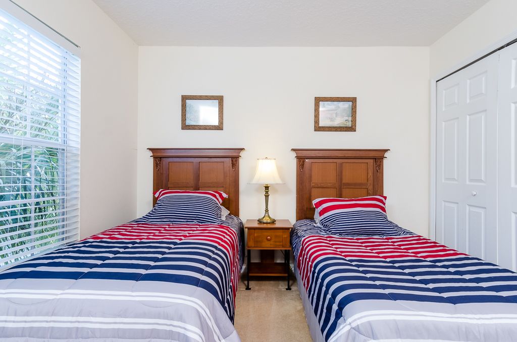 A bedroom with two beds, a nightstand, a lamp, and a window with blinds.