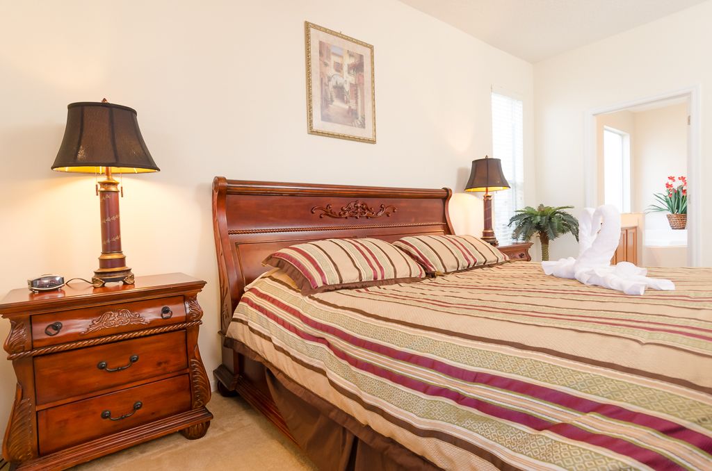 A neatly made bed with striped bedding, a wooden nightstand with a lamp, and a framed picture on the wall.