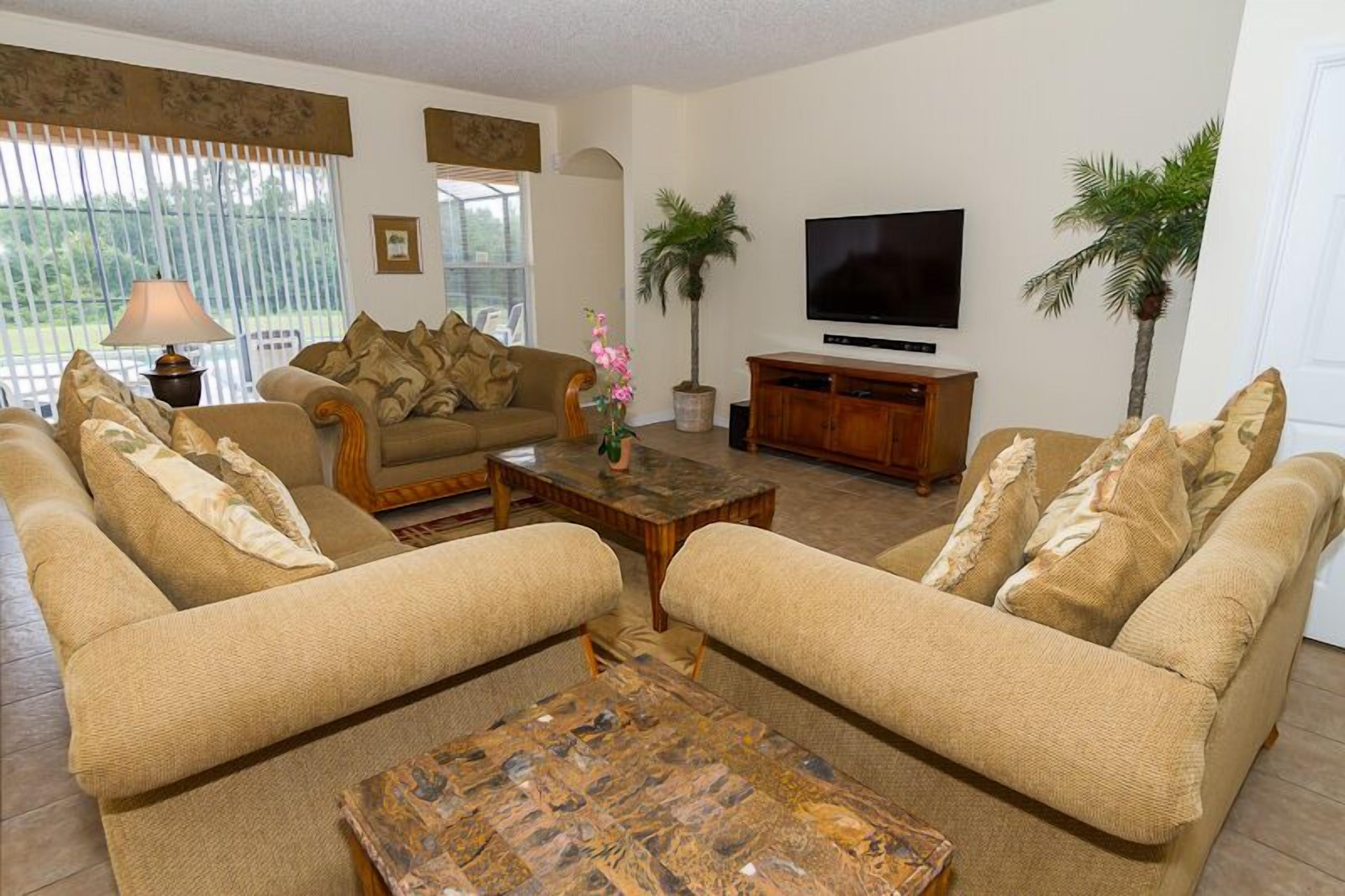 A living room with two beige sofas, a coffee table, a TV, and a potted plant.