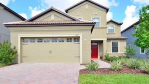 Un immeuble résidentiel de deux étages avec un garage de couleur beige, une porte rouge et une allée pavée en briques.