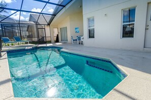 A swimming pool with a glass enclosure, a covered patio area, and a white building with a door and windows. - Ov1030 - Emerald Island - 4 Bed 3 Baths Townhome (Kissimmee)
