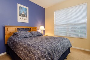 A bedroom with a bed, a nightstand, a lamp, and a window with blinds. - Ov1030 - Emerald Island - 4 Bed 3 Baths Townhome (Kissimmee)