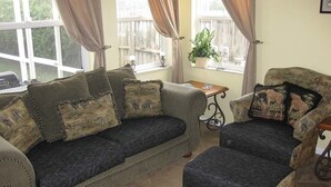 A cozy living room with a sofa and armchair, a small table, and a window with curtains. - Ov2672 - Lindfields - 4 Bed 3 Baths Villa (Kissimmee)