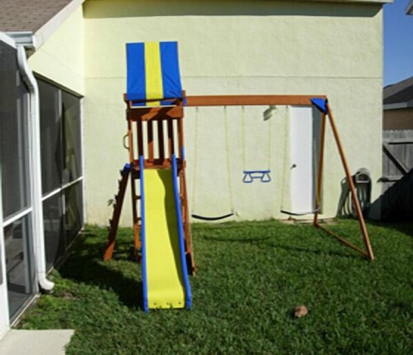 A wooden swing set with a yellow slide in a backyard.