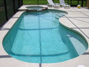 A swimming pool with a hot tub, surrounded by lounge chairs and a sunshade.