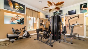 Un gimnasio con equipo de ejercicio, ventilador de techo y obras de arte en las paredes.