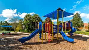Un parque infantil con toboganes y estructuras para escalar, rodeado de árboles y un cielo despejado.