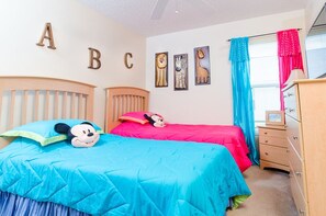Une chambre d’enfant avec deux lits, des décorations représentant l’alphabet sur le mur et un doudou à l’effigie de Mickey Mouse sur le lit de gauche.