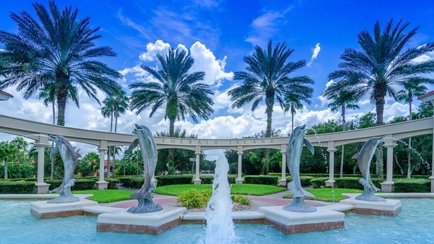Une fontaine ornée de dauphins, de palmiers et surplombée d’un ciel bleu azur.