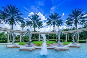 Une fontaine ornée de dauphins, de palmiers et surplombée d’un ciel bleu azur.