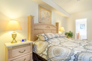 Ein Schlafzimmer mit einem Bett, zwei Nachttischen mit Lampen, einem Beistelltisch, einem gerahmten Bild an der Wand und einer Topfpflanze.