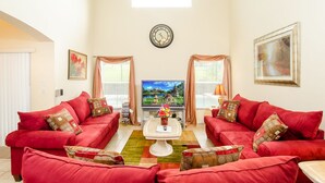 Ein Wohnzimmer mit zwei roten Sofas, einem Couchtisch, einem Fernseher und einer Uhr an der Wand.
