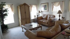 A living room with a beige sofa, a coffee table, and a cabinet. There is a painting on the wall and a lamp on a side table. - Ov4069 - Vista Park - 5 Bed 4 Baths Villa (Davenport)