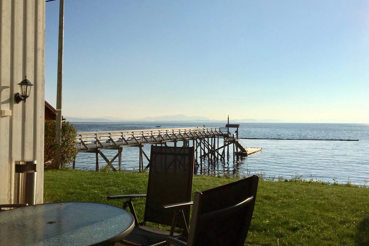 Un patio con una mesa y sillas que da a un cuerpo de agua y un muelle.