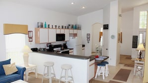 A compact kitchen with a central island, bar stools, and a dining area with a table and chairs. - Ov3868 - Hampton Lakes - 5 Bed 3 Baths Townhome (Davenport)