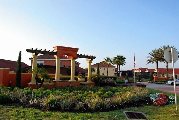A landscaped area with a pergola structure, palm trees, and a flagpole.