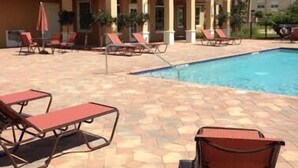 Un espace aménagé au bord de la piscine, avec des chaises longues, et un bâtiment doté d’un toit recouvert de tuiles.