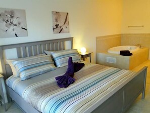 Una habitación de hotel con una cama, una mesita de noche, un lavamanos empotrado en la pared y dos cuadros abstractos.