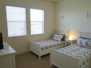 A bedroom with two single beds, a desk, and two windows.