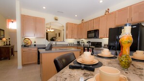 A modern kitchen with wooden cabinets, a granite countertop, and a dining area set for four.