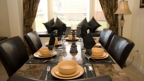 A dining table set for six with black chairs, a candle centerpiece, and a window with blinds in the background.