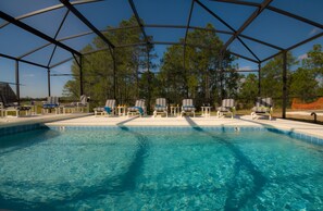 Un área de piscina con zona de estar cubierta y sillones de descanso.
