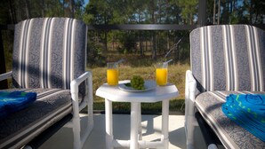 A deck with two striped chairs, a small table with a plate of grapes and two glasses of orange juice, and a blue towel on one chair.