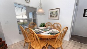A dining area with a round table, six wooden chairs, and a ceiling light fixture.