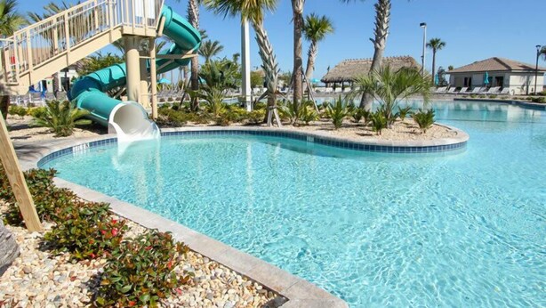 Una piscina con tobogán de agua, palmeras y un edificio con techo de paja.