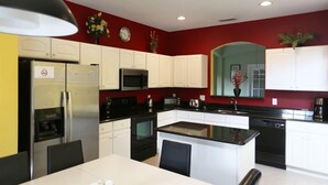 Una cocina moderna con gabinetes blancos, un refrigerador negro, un microondas y una cafetera.
