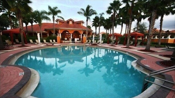 Una piscina circular con un deck de baldosas rojas, rodeada de palmeras y sillones de descanso.