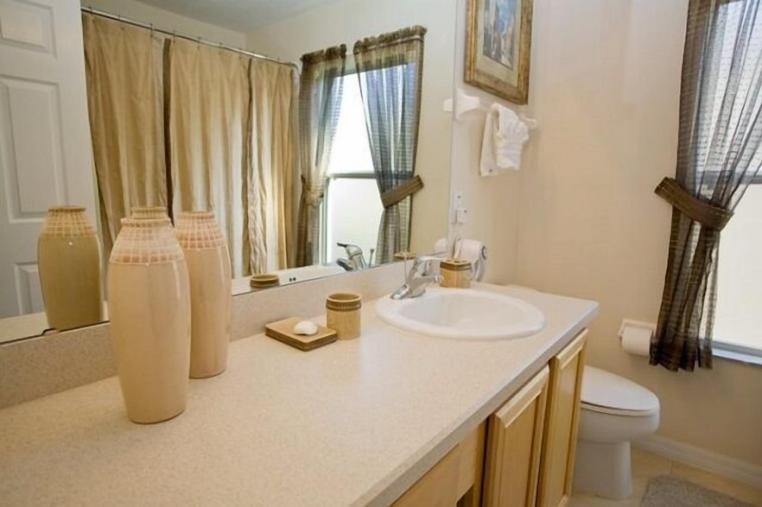 A bathroom with a white sink, beige countertop, and a mirror. There are three beige vases on the counter.