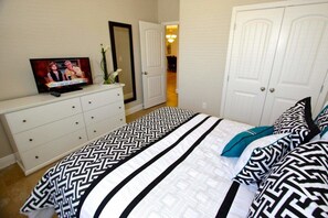 A bedroom with a bed, dresser, TV, and two doors.